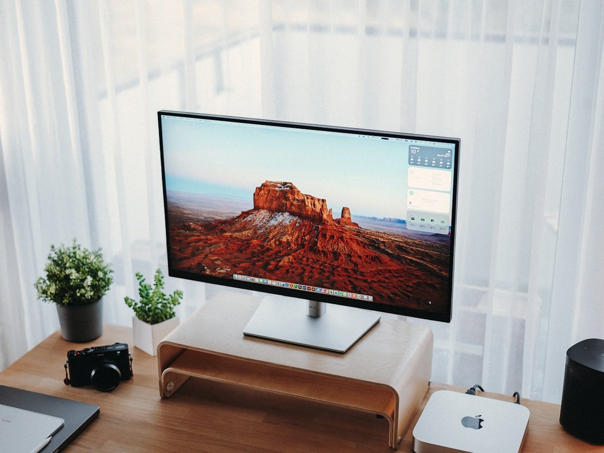 Walnut monitor stand on a white desk with keyboard and felt mat